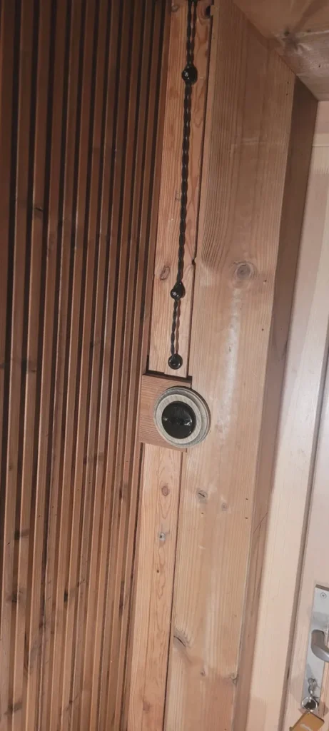 Juodas keramikinis jungiklis ant medinės sienos su tekstiliniu laidu