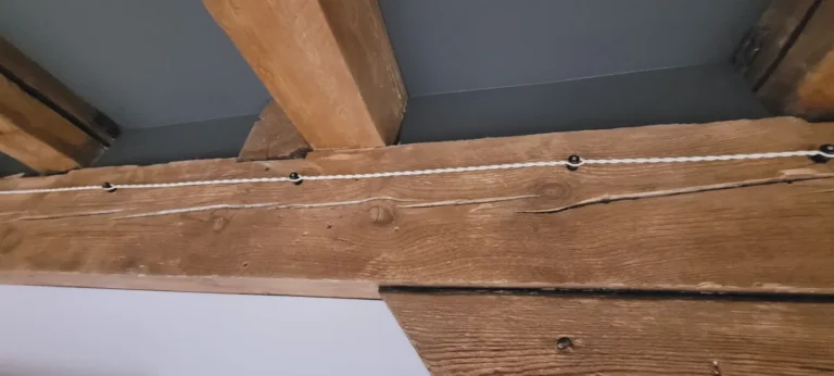 Baltas tekstilinis laidas ant izoliatorių per seną medinę siją