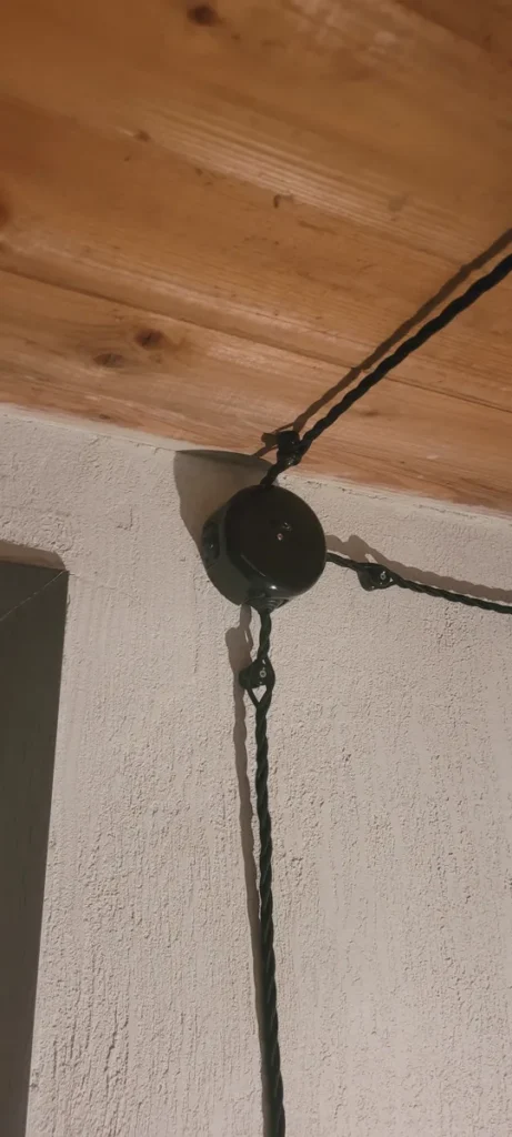 Juodas tekstilinis laidas ir keramikinė paskirstymo dėžutė po lubomis