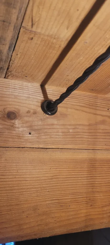 Juodas pintas tekstilinis laidas per įvorę medinėse lubose