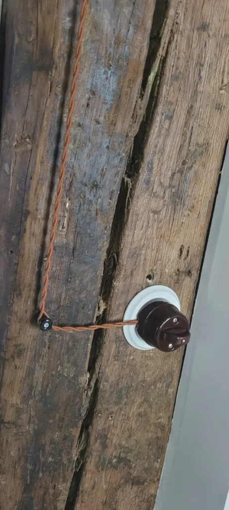 Rudas tekstilinis laidas prie porcelianinio jungiklio ant senos sijos