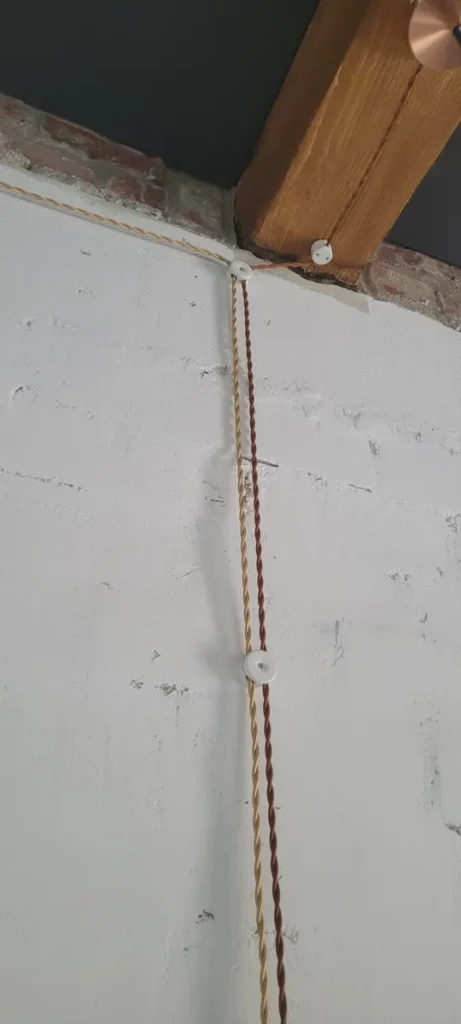 Aukso ir rudas tekstiliniai laidai ant baltų izoliatorių