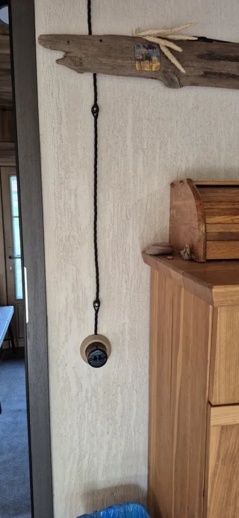 Juodas tekstilinis laidas ant izoliatorių iki retro jungiklio